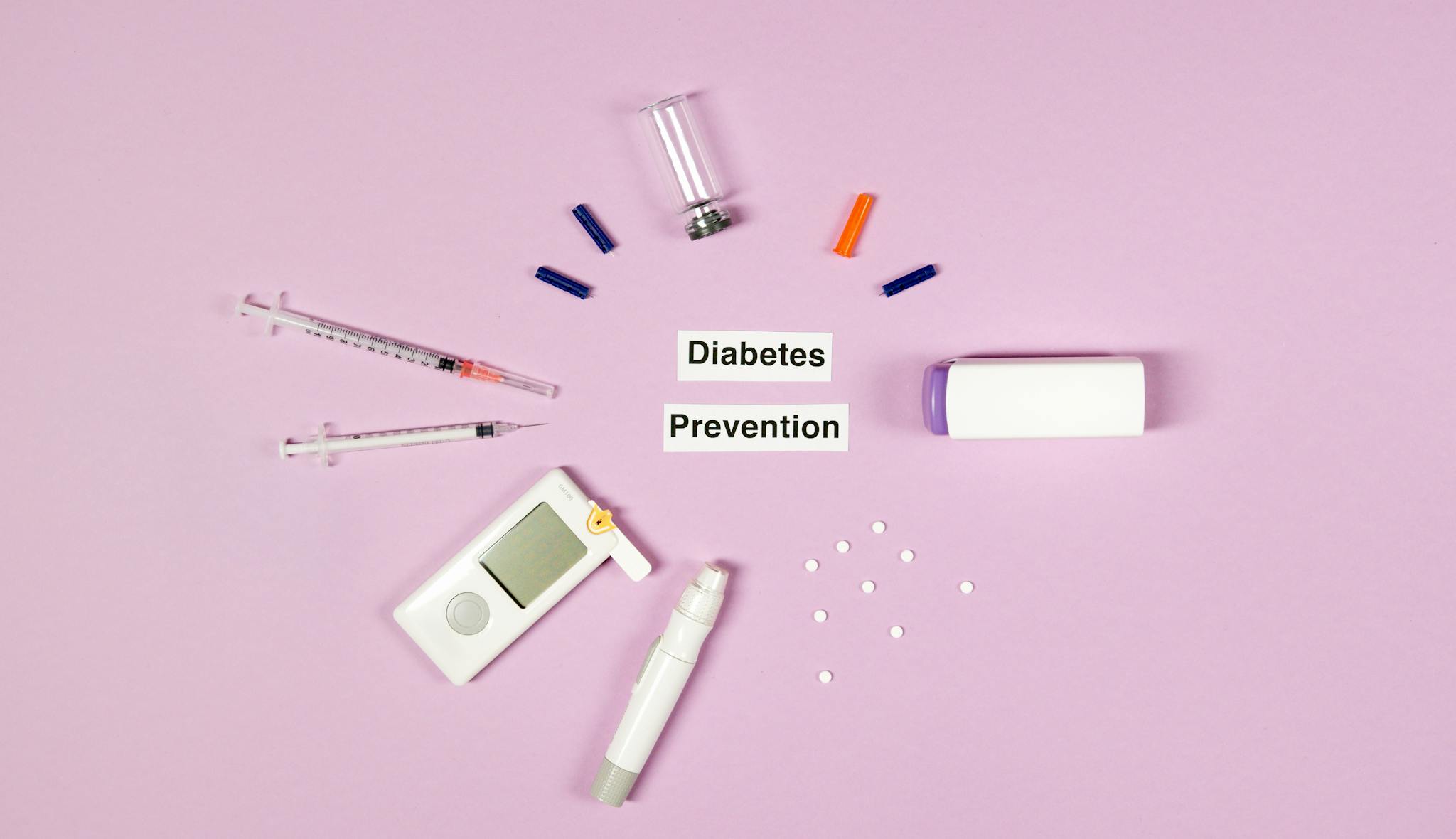 A flat lay of diabetes prevention supplies including a glucometer, insulin pen, and syringes on a pink background.